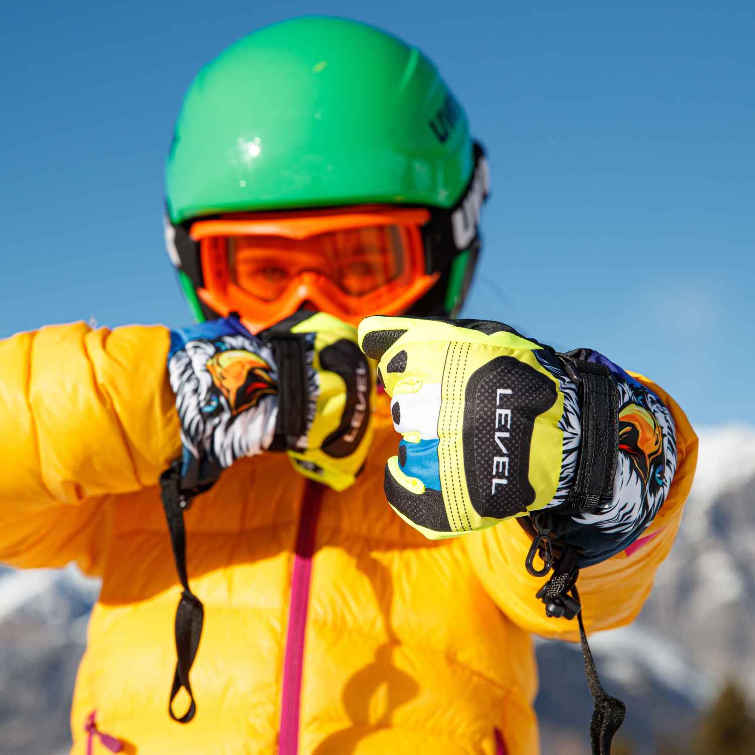 A child standing in the snow wearing ski gloves, puffy jacket and ski goggles about to go skiing.