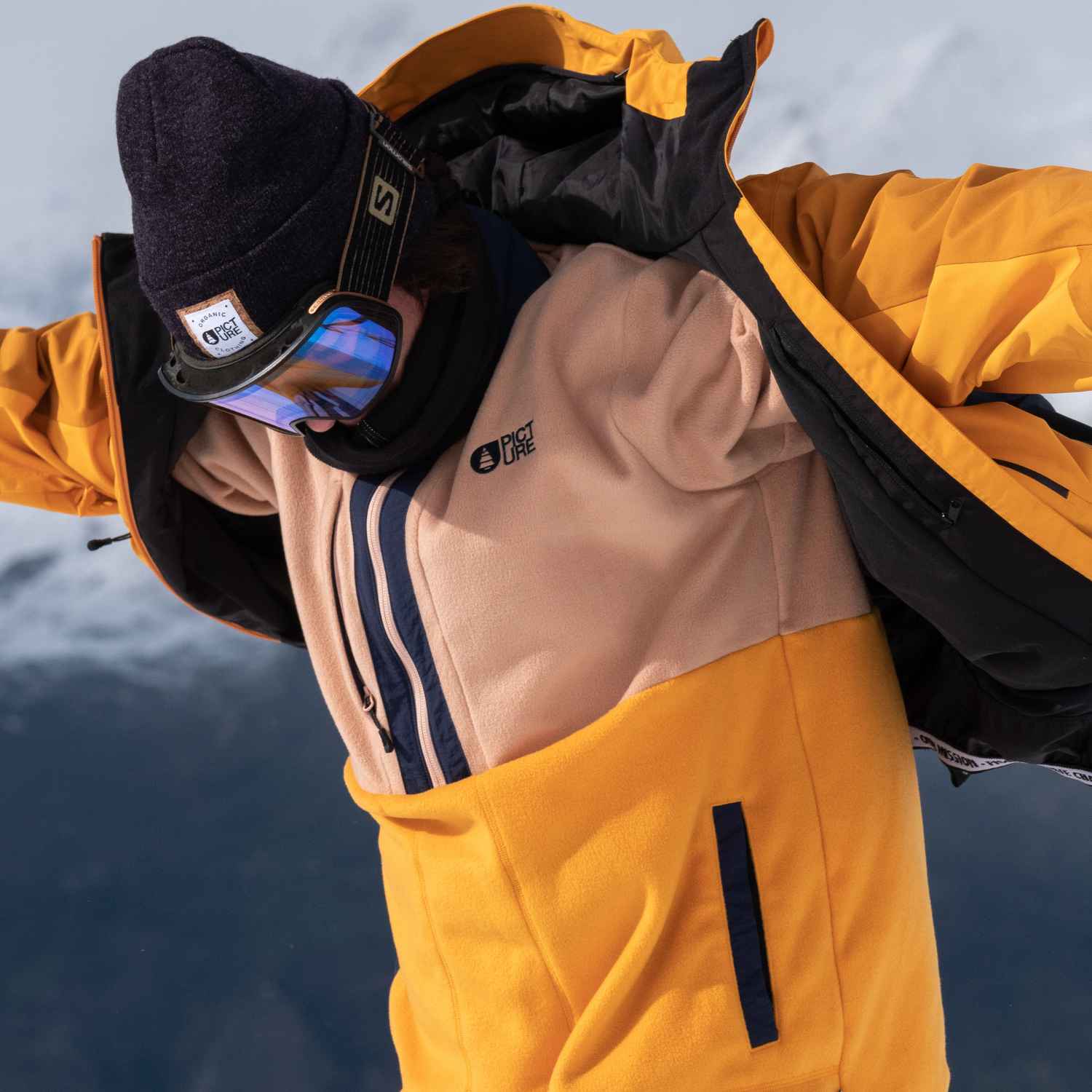 A range of ski clothing including a ski jackets, ski pants and ski goggles on man in the snow.