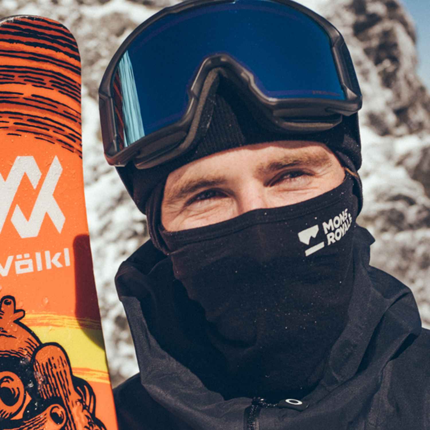 A man wearing a neck warmer and ski goggles, in the snow, about to go skiing. 